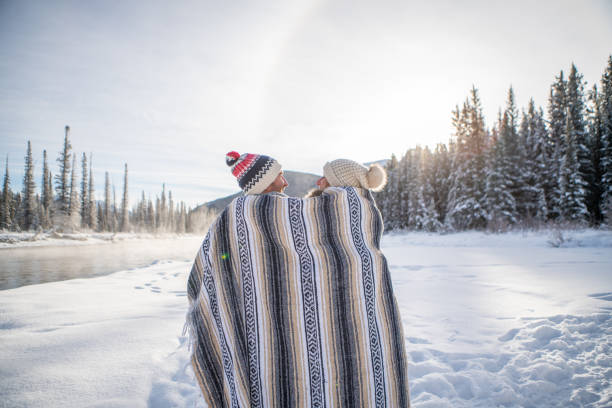 istock Couple sitting in snow by the river wrapped in blanket 1175944355