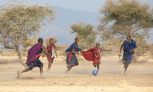 Arusha, Tanzania, 7th September 2019: maasai men playing football in dusty savannah