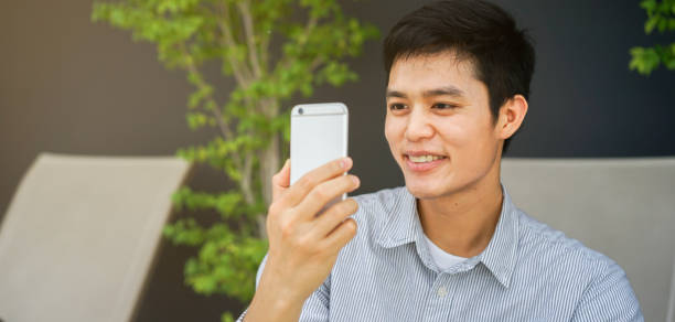istock close up young asian man holding smartphone and using front camera to video conference with friends on 4g LTE telecommunication network at outside resort in weekend holidays , millennial lifestyle concept 1175961859