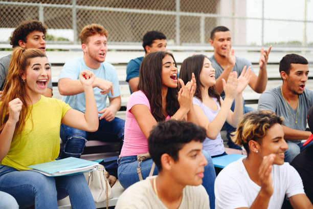 Supportive Hispanic students cheering for high school team Group of enthusiastic Hispanic teenage students sitting in high school bleachers and applauding their team. school bleachers stock pictures, royalty-free photos & images