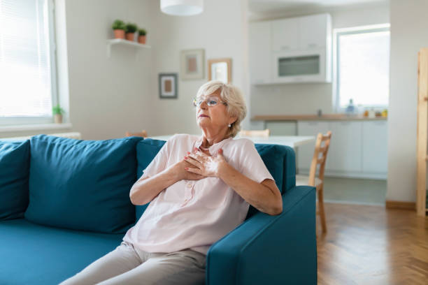 Heart problems can affect anyone at any time Senior Woman Suffering From Chest Pain While Sitting on Sofa at Home. Portrait of Elderly Woman Having Heart Attack symptom photos stock pictures, royalty-free photos & images