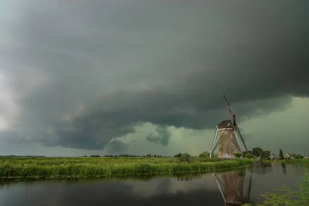 Typical dutch scene with a windmill along the waterside. A green sky of an approaching thunderstorm, indicative of hail.