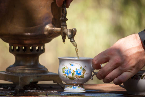 istock Male hand pours tea from an antique bronze wood burning samovar into a cup on a rusty table outdoor, selective focus 1175978902