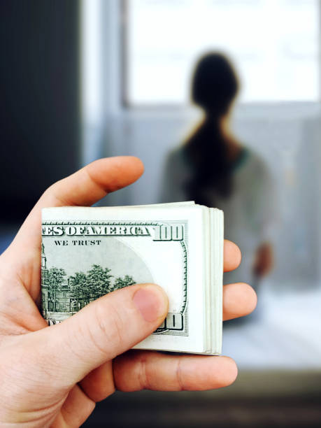 Man holds in his hand a bundle of one hundred dollar bills against the background of the girl who they are going to sell into slavery. The concept of violence, human trafficking. Mixed media stock photo