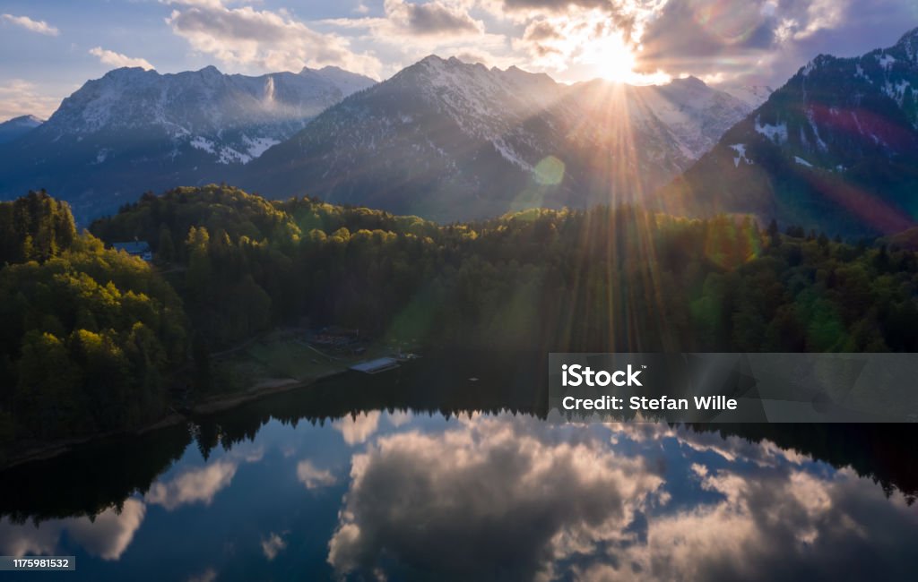 Sunrise at Freibergsee lake near oberstdorf reclecting clouds on the water surface of the lake and a sunstar Allgau Stock Photo