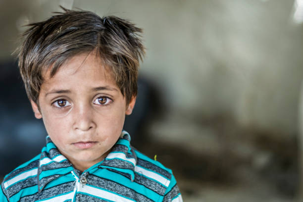 primo piano di un povero orfano affamato che fissa in un campo profughi con una triste espressione sul viso e il viso e i vestiti sono sporchi e i suoi occhi sono pieni di dolore - povertà asia foto e immagini stock