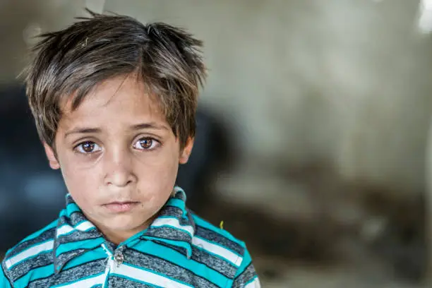 Photo of closeup of a poor staring hungry orphan boy in a refugee camp with sad expression on his face and his face and clothes are dirty and his eyes are full of pain