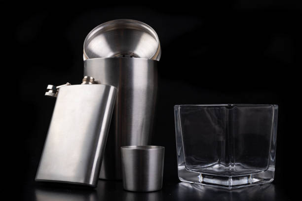 istock Metal shaker, hip flask and vodka glass. Bartender accessories on the table. Black background. 1175996454