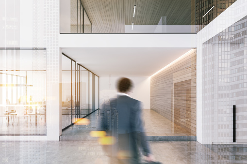 Businessman entering modern office with white and wooden walls, concrete floor and conference room with glass doors. Toned image double exposure blurred