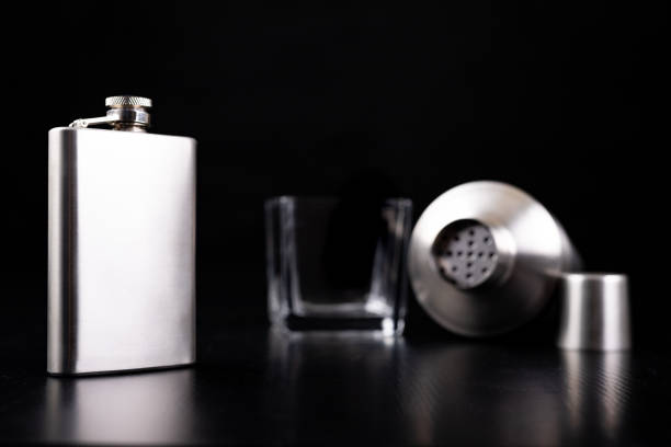 istock Metal shaker, hip flask and vodka glass. Bartender accessories on the table. Black background. 1175996539