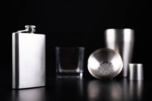 istock Metal shaker, hip flask and vodka glass. Bartender accessories on the table. Black background. 1175997784