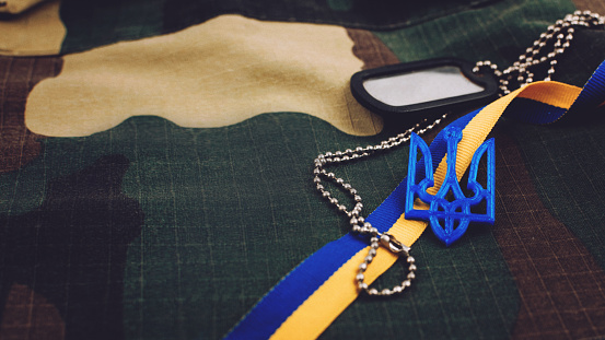 Ucrania antecedentes militares . Símbolos nacionales ucranianos, escudo de armas tridente, cinta amarilla y azul, ficha en el fondo uniforme militar.