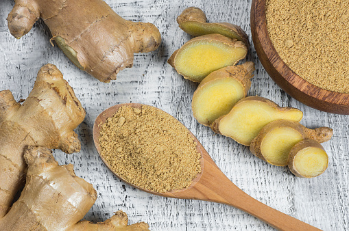 Fresh chopped ginger root and ground ginger powder in wooden spoon on wooden rustic table. Healthy food spice concept. Zingiber officinale