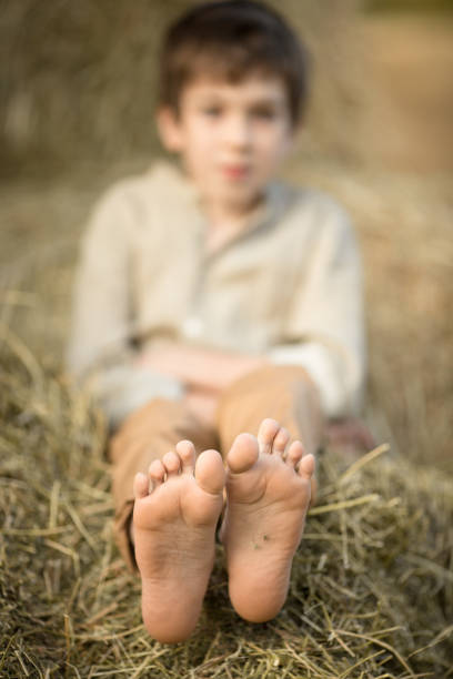 A Farm Boy in the Russian Countryside is taking a much needed rest break.  He's kicked off his shoes and is relaxing barefoot on the hay piles.