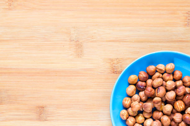 Hazelnut in blue plate on wooden background. Hazel nut for food. Organic food rustic banner template with text space. Tasty healthy snack. Scattered hazel nut on table top view. Hazelnut pile flat lay