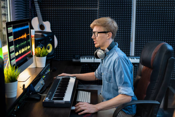 istock Young deejay in denim shirt looking at sound mixing tracls on computer screen 1176082543