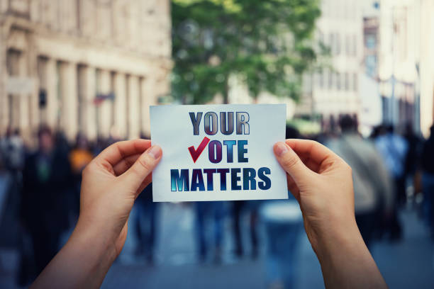 手は、混雑した通りの背景の上にあなたの投票が重要なメッセージと紙シートを保持します。人々は法的および民主的な権利、すべての声が重要です。選挙運動と選挙扇動の概念 - 投票 ストックフォトと画像