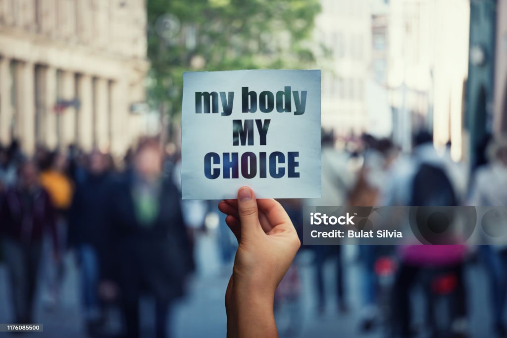 Feminist hands holding a protest banner with the message my body my choice over a crowded street. Human rights concept against fetus law and reproductive justice. Stop discrimination and injustice Feminist hands holding a protest banner with the message my body my choice over a crowded street. Human rights concept against fetus law and reproductive justice. Stop discrimination and injustice. Choice Stock Photo