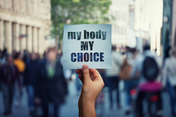 Feminist hands holding a protest banner with the message my body my choice over a crowded street. Human rights concept against fetus law and reproductive justice. Stop discrimination and injustice Feminist hands holding a protest banner with the message my body my choice over a crowded street. Human rights concept against fetus law and reproductive justice. Stop discrimination and injustice. reproductive rights stock pictures, royalty-free photos & images