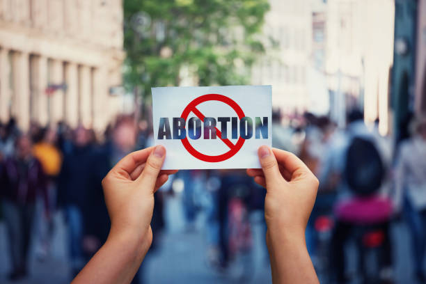 istock Activist hands holding a banner with stop abortion message over a crowded street background. Social awareness concept, humanity problems say no to abortion. Fetus rights law and reproductive justice 1176085645