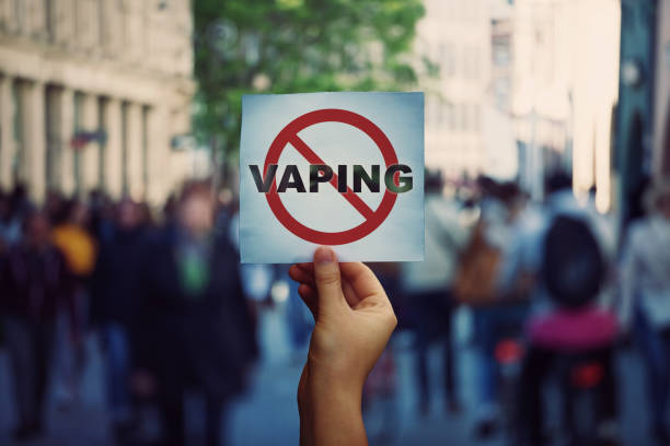 Human hand holding a protest banner stop vaping message over a crowded street background. Banning flavored vaping products to discourage people from smoking electronic cigarettes. Health risk concept. Human hand holding a protest banner stop vaping message over a crowded street background. Banning flavored vaping products to discourage people from smoking electronic cigarettes. Health risk concept. harm stock pictures, royalty-free photos & images