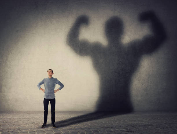 valiente adolescente enfrentando sus miedos como un héroe poderoso. chico lanzando una fuerte sombra de culturista muscular, mostrando grandes bíceps. autodefensa, fuerza interior y concepto de motivación y confianza. - strong shadows fotografías e imágenes de stock