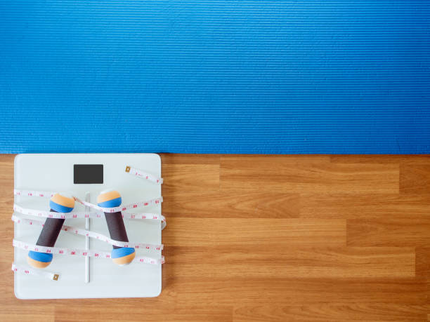 istock weight loss and physical activity concept from weight scale digital with measure tape for check body shape and workout equipment on a wooden floor. 1176087276