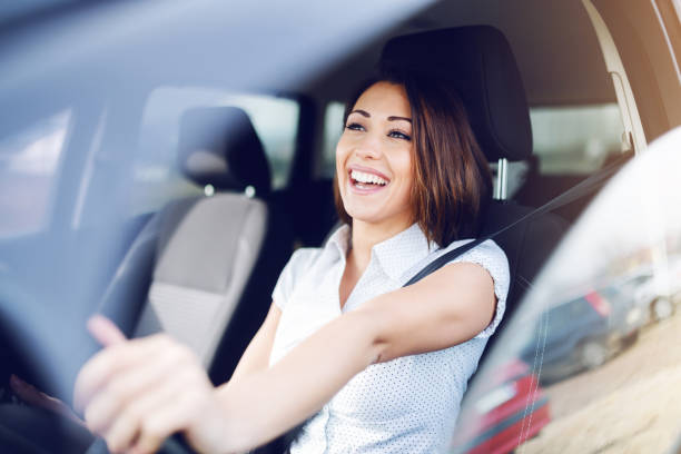 attraktiva leende kaukasiska brunett kör sin bil. händerna är på ratten. - car driver bildbanksfoton och bilder