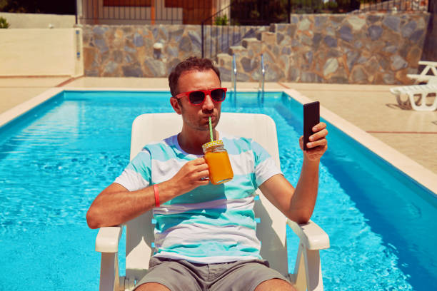 istock Attractive man using cellphone while drinking juice near swimming pool. 1176095924