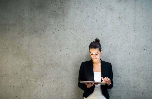 jeune femme d'affaires avec la tablette restant contre le mur en béton dans le bureau. - simplicity using computer women computer equipment photos et images de collection