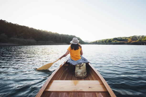 Rear view of canoeist girl Rear view of hipster girl paddling the canoe on the sunset lake. using a paddle stock pictures, royalty-free photos & images