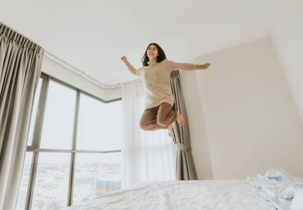 istock Asian woman excited jumping on her bed 1176102351