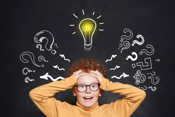 istock Little boy with red ginger hair against blackboard background with lightbulb 1176102852