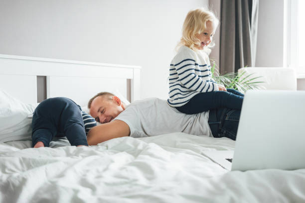 istock Tired father sleep but his children interferes him. Young happy father lying on bed while his daughter play with him 1176103376