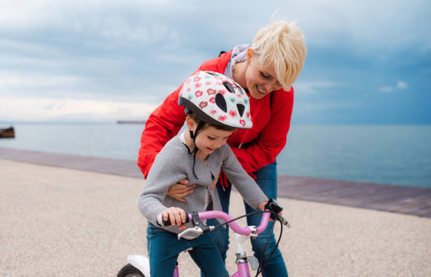 istock Mother helping small daughter to ride bicycle outdoors on beach. 1176105412
