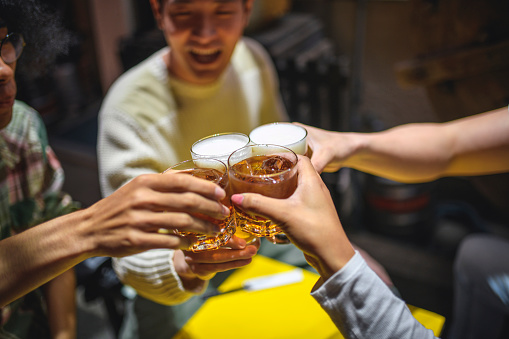 High angle close-up of four friends raising glasses in celebratory toast at table outside Tokyo izakaya.