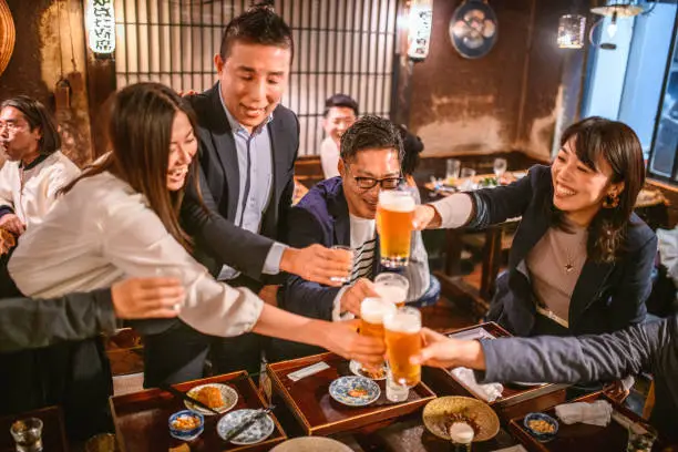 Carefree Japanese couples in 30s and 40s raising beer glasses to toast good fortune at Tokyo izakaya.