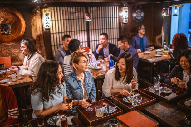 High Angle View of Female Friends Sitting at Tokyo Sushi Bar Wide angle view of Mongolian, Japanese, and Caucasian women sitting at sushi bar and other patrons in Tokyo izakaya. central asian ethnicity stock pictures, royalty-free photos & images