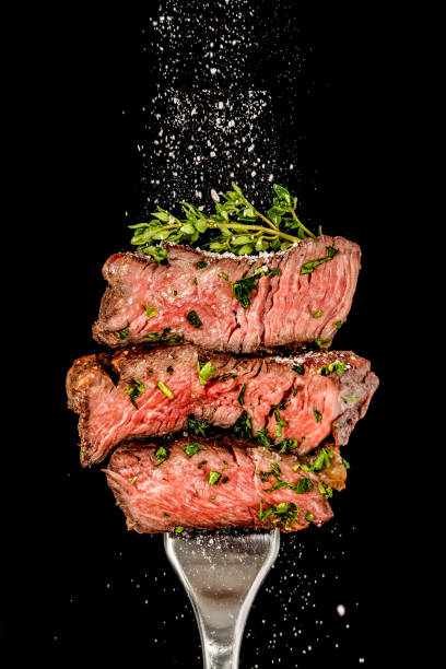 Sliced beef steak from grill on a fork. Salt is strewing from above stock photo