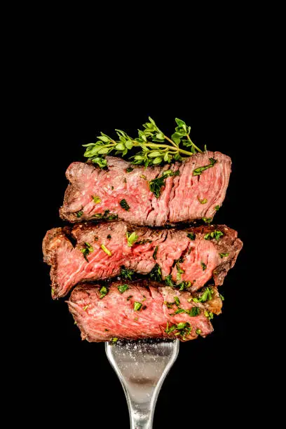 Slices of grilled beef steak with herbs  on a fork.  Black background
