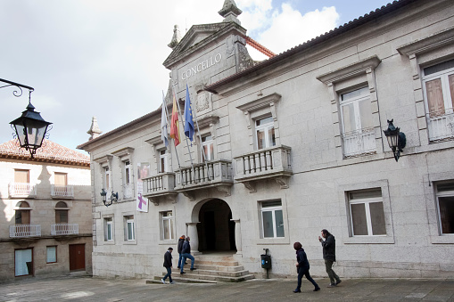 Tui, Spain- November 30, 2018: Facade of Town hall in Tui, Pontevedra province, Galicia, Spain seen from town square . Casual people walking, balcony with flags, old-fashioned street light.