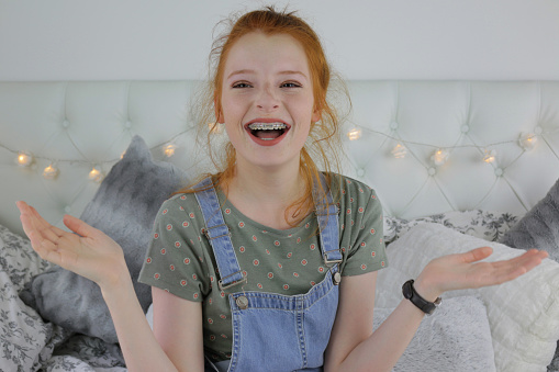 Stock photo showing a close-up of a beautiful, ginger haired teenager modelling a natural makeup look and a denim pinafore dress over a green patterned t-shirt.