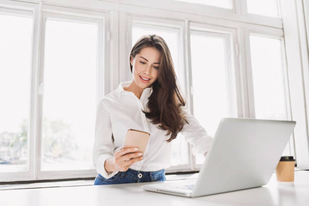 hermosa mujer de negocios usando computadora portátil y teléfono inteligente - on the phone women beautiful beauty fotografías e imágenes de stock