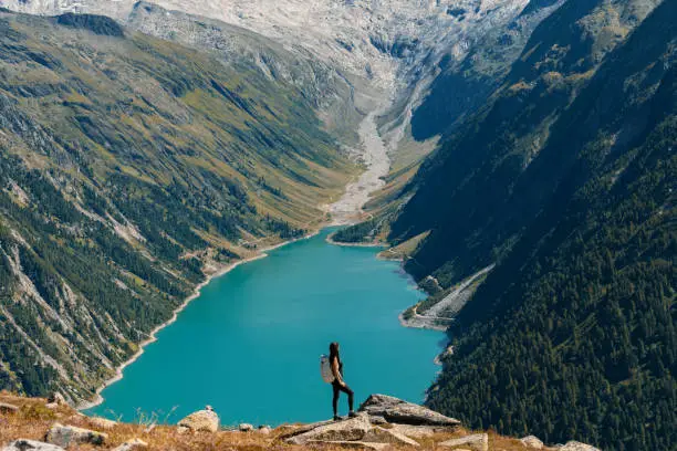 Beautiful alpine landscape with young woman standing in backpack and azure mountain lake in the background, Zillertal Alps, Austria