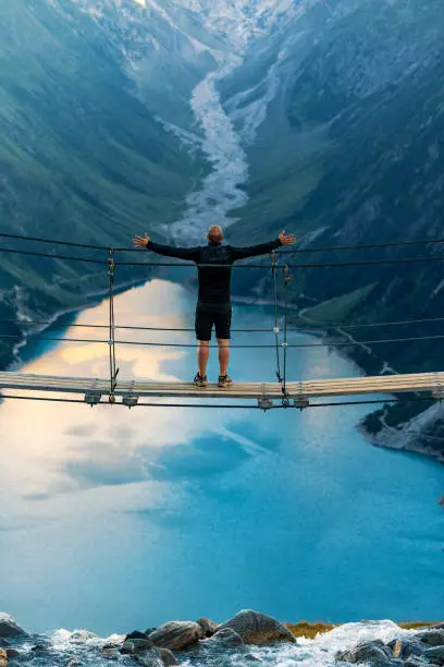 Man standing with open arms while Hiking at Lake Schlegeis, Zillertal Alps, Austria, standing at the bridge.