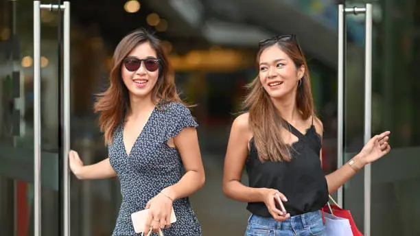 Two friends woman open door with shopping mall and smiling while carry shopping bags.