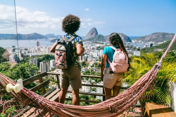 Young Brazilian couple looking at Sugarloaf Mountain, wearing backpacks, on gap year