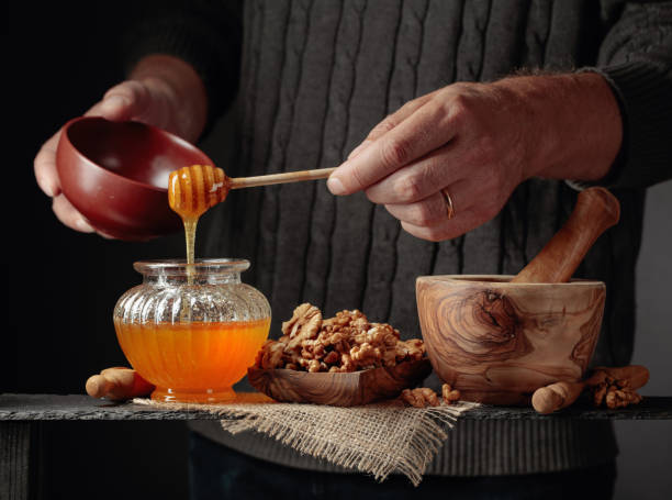 el hombre de un suéter prepara un desayuno de nueces y miel. - mortar and pestle wood healthcare and medicine jar fotografías e imágenes de stock