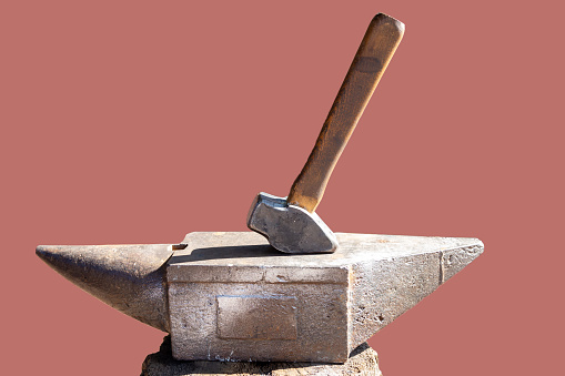 Rusty black blacksmith anvil and a hammer isolated on pink background