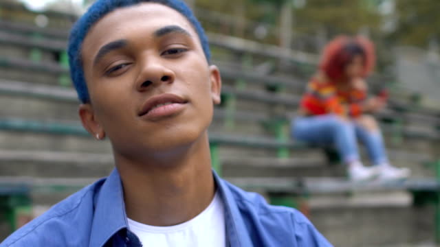 Self-confident blue-haired black teen guy smiling on camera, adolescence age